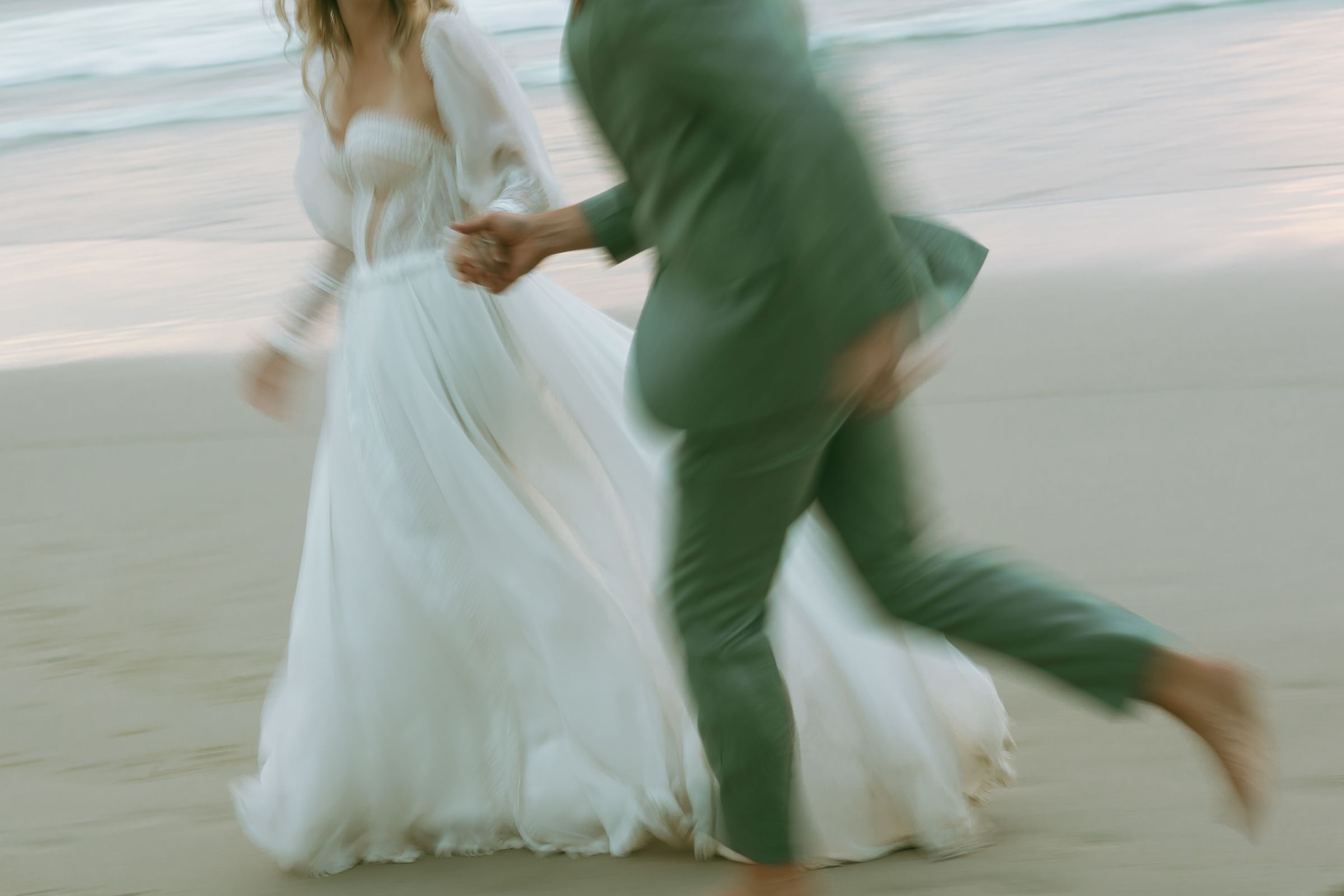 Bride and groom running hand in hand along the beach