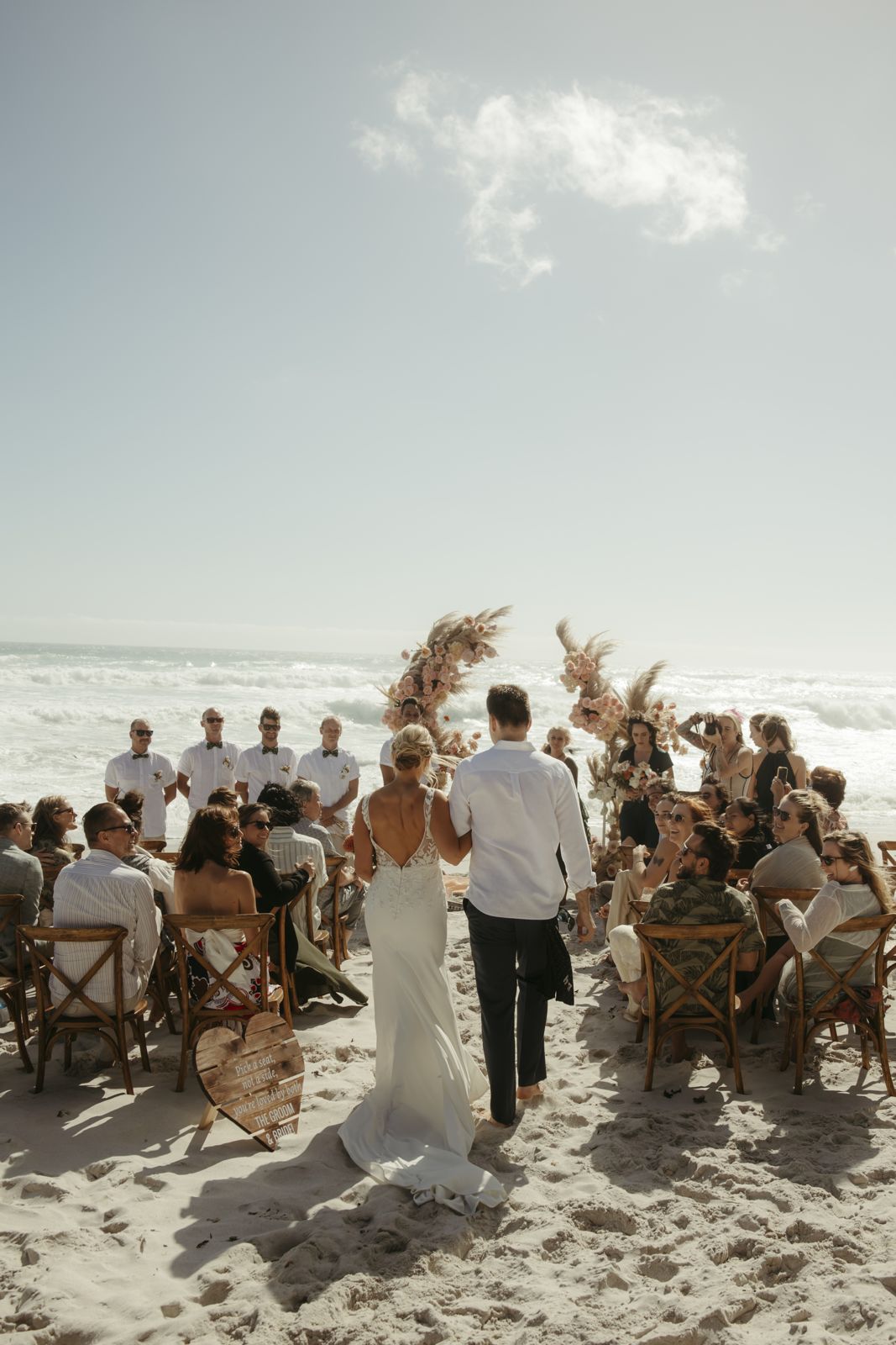 Beach ceremony with guests and dried-flower arches