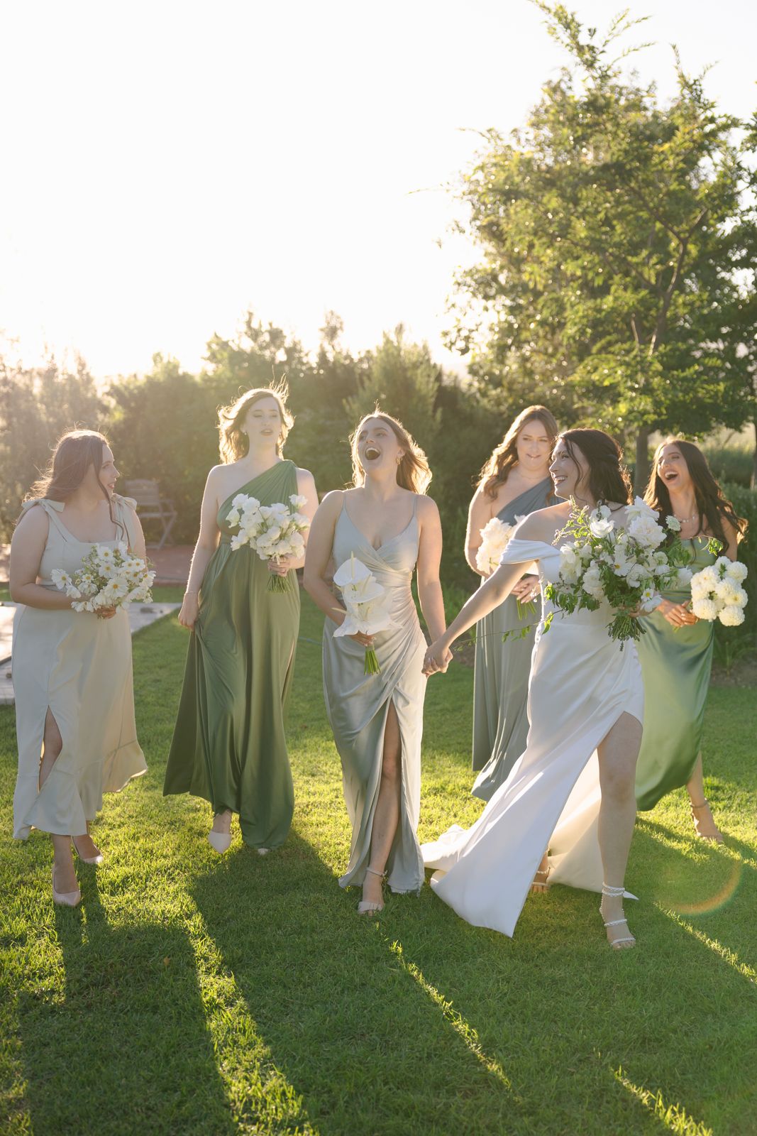 Bridesmaids in sage dresses walking across a lawn