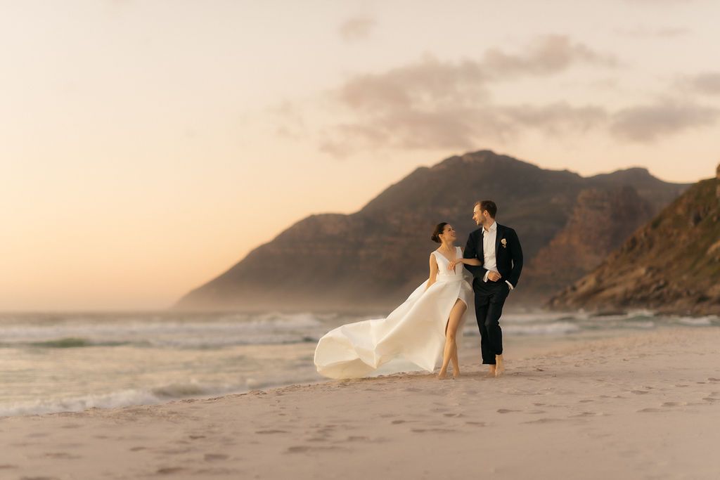 Couple walking along the beach at sunset below the mountains
