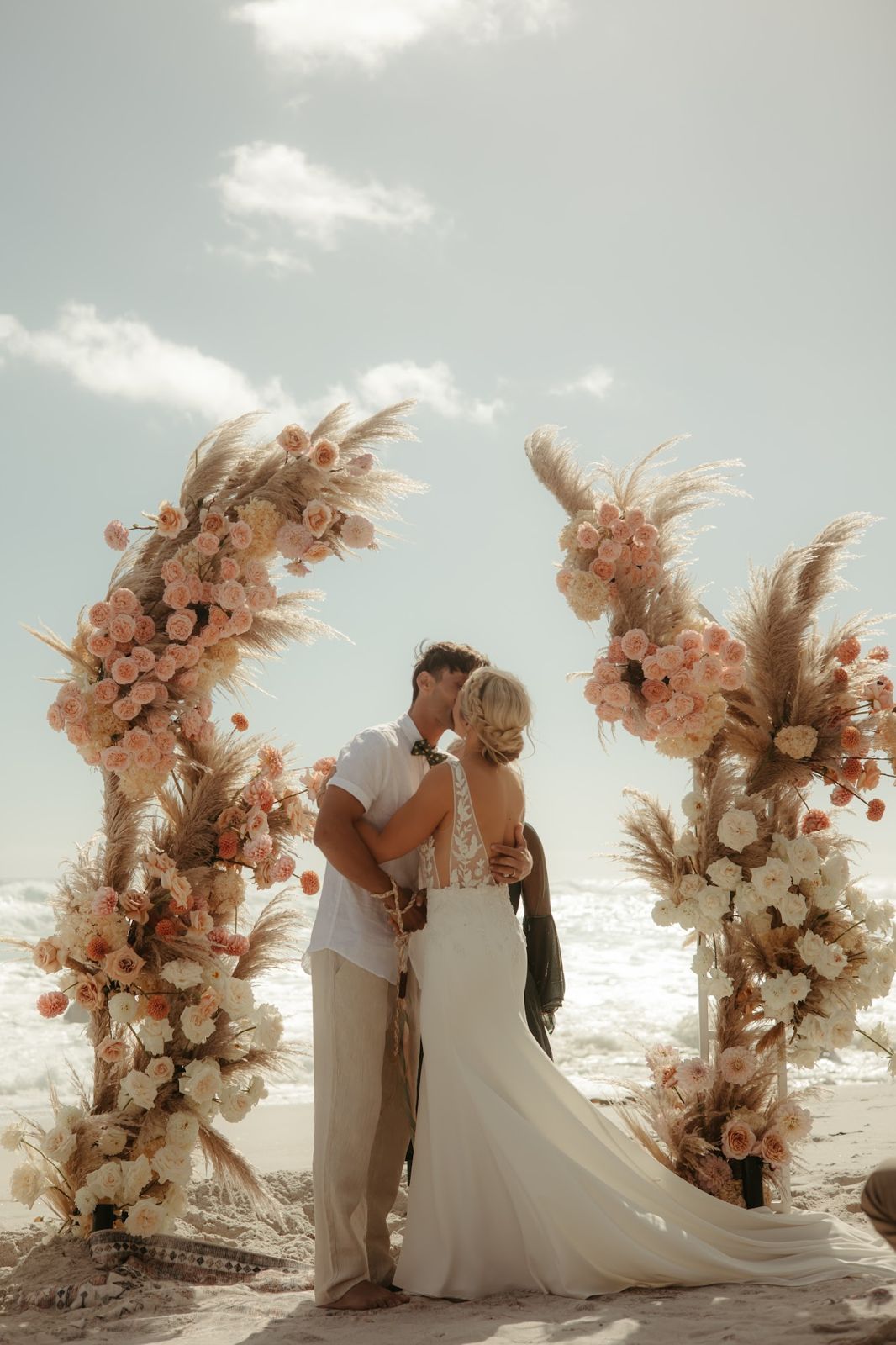 Couple kissing beneath a pampas and rose arch on the beach