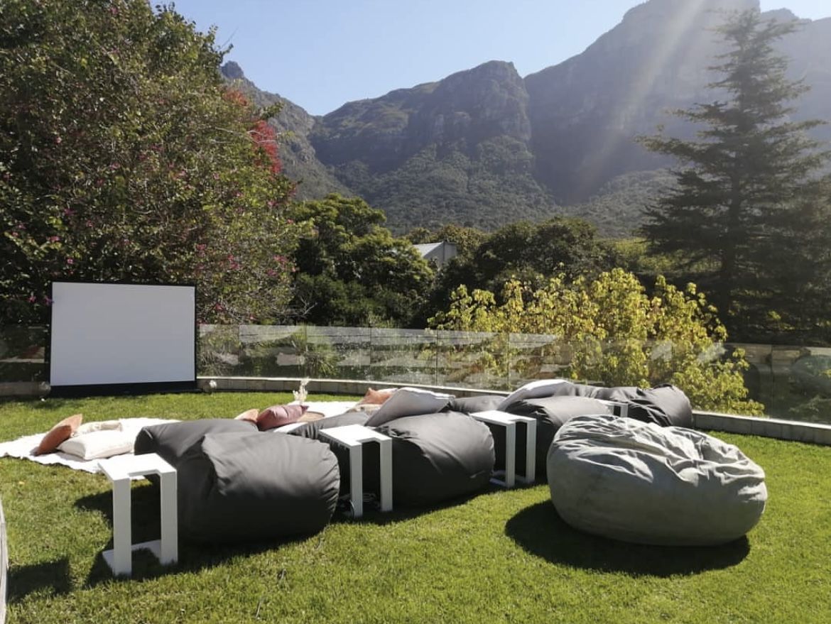 Bean bags facing a cinema screen on a lawn below the mountain