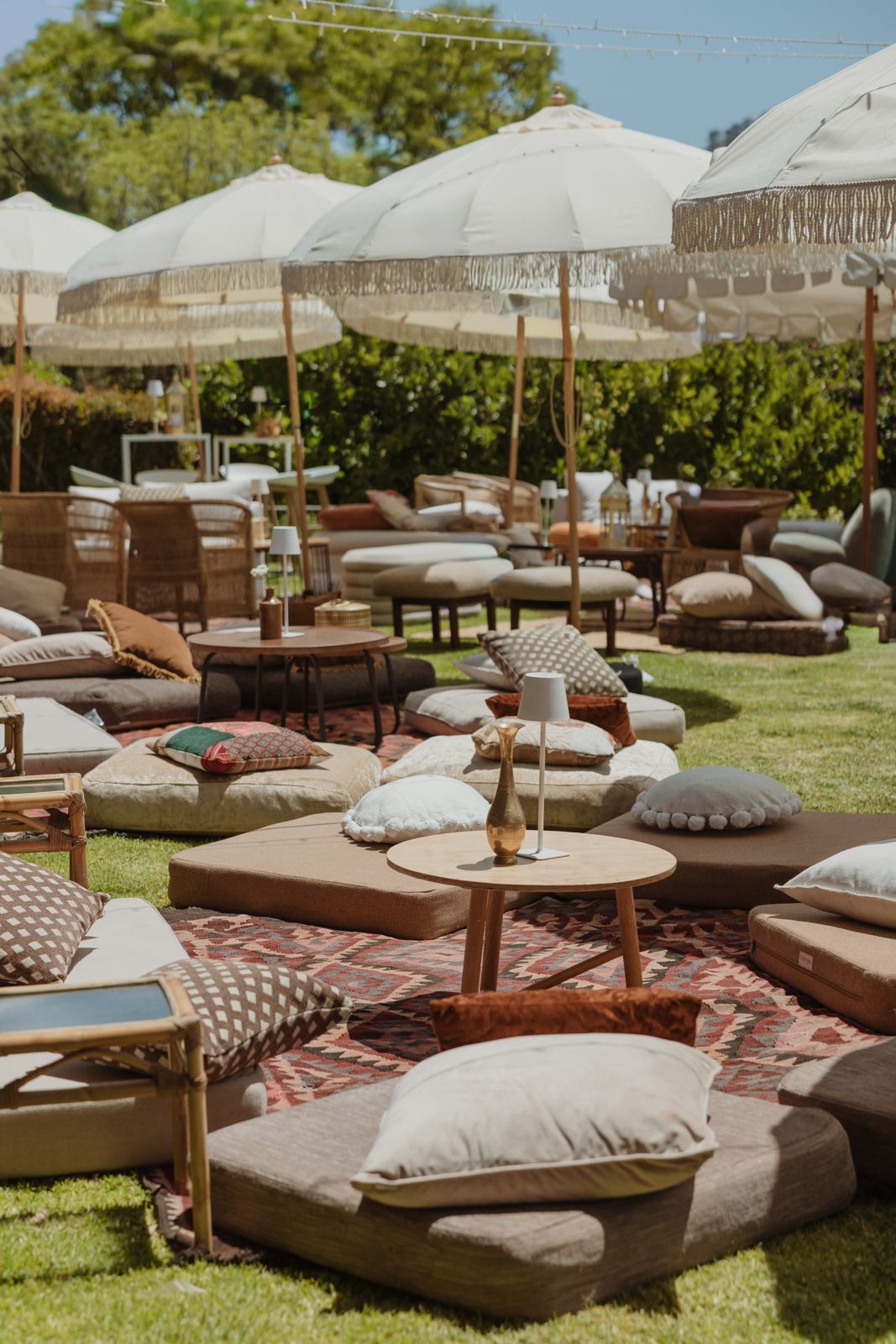 Lounge of floor cushions, rugs and fringed umbrellas on a lawn