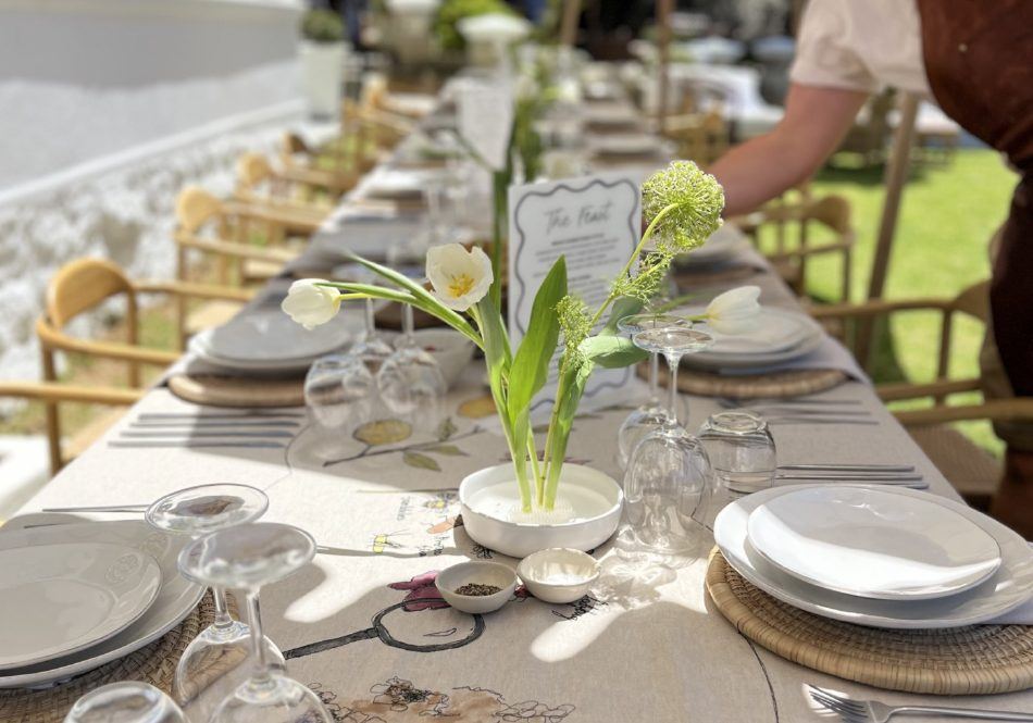 Long table laid for lunch with white plates and bud vases